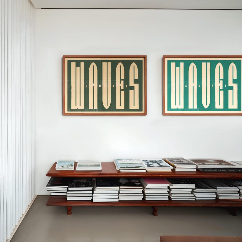 May include: Two framed prints with the word "WAVES" in a bold, graphic font. The prints are hung on a white wall above a wooden shelf filled with books.