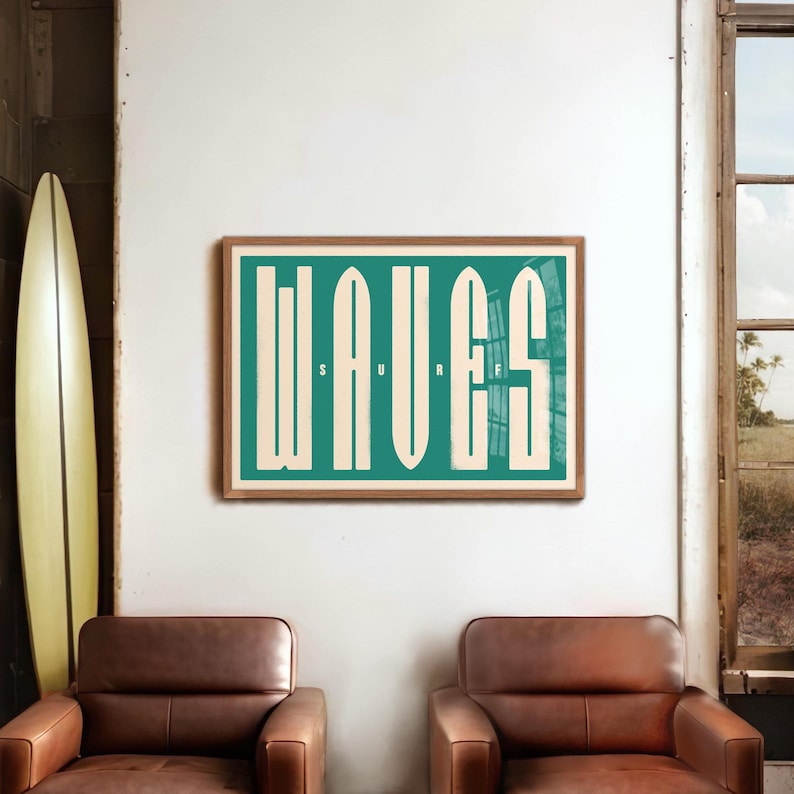 May include: A framed print with the word "WAVES" in large, white letters on a teal background. The letters are stylized to look like waves. The print is hanging on a white wall in a room with two brown leather armchairs and a surfboard.