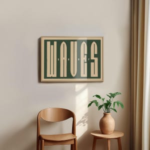 May include: A framed print with the word "WAVES" in a stylized font, with the word "SURF" written in smaller letters below. The print is on a green background with cream-colored letters. The print is hanging on a beige wall.