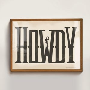 K&ouml;nnte beinhalten: Ein gerahmter Druck mit einem schwarz-wei&szlig;en Design des Wortes "HOWDY" mit einer Silhouette eines Cowboys, der auf dem "W" steht.