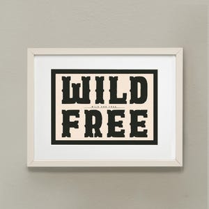 May include: A white framed print with black text that reads "WILD AND FREE" in a bold, vintage font.