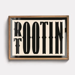 May include: A framed print with the word "ROOTIN'" in black text on a cream background. The frame is made of wood and has a dark brown finish.