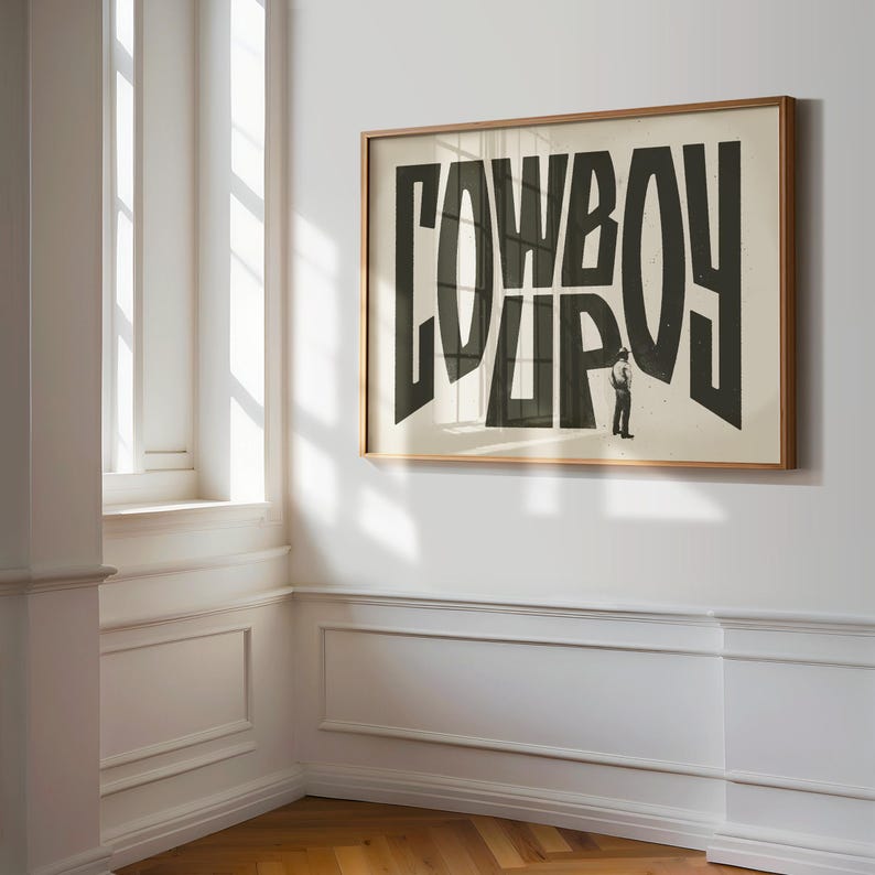 May include: A framed print with the word "COWBOY" in large, black letters. The letters are stacked on top of each other, and a small figure of a person is standing in the middle of the word.