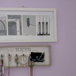 Pu&ograve; includere: Due opere d'arte incorniciate sono appese a una parete color lavanda. La cornice superiore contiene quattro immagini in bianco e nero. La cornice inferiore &egrave; un organizer per gioielli con la scritta "KEYS" e diverse collane e orecchini appesi.