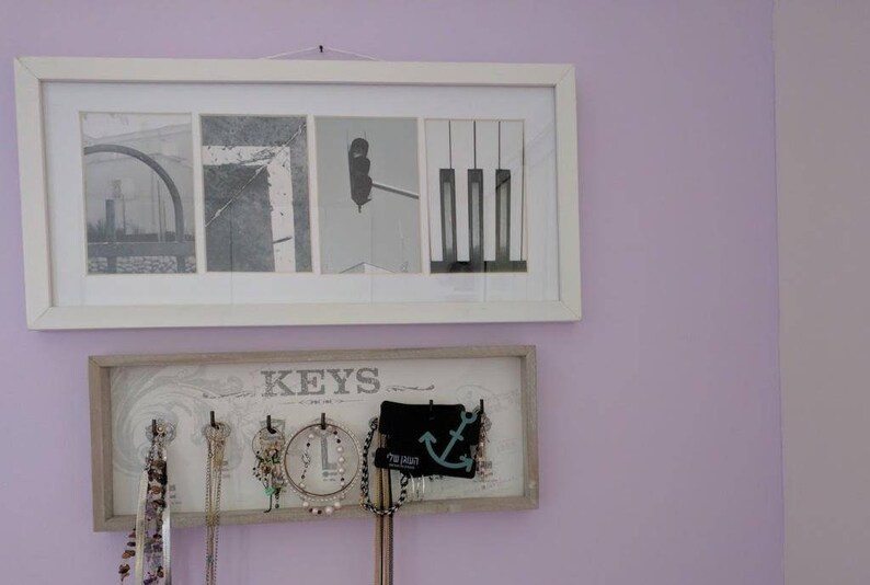 Pu&ograve; includere: Due opere d'arte incorniciate sono appese a una parete color lavanda. La cornice superiore contiene quattro immagini in bianco e nero. La cornice inferiore &egrave; un organizer per gioielli con la scritta "KEYS" e diverse collane e orecchini appesi.
