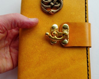 May include: A yellow leather journal with a gold clasp and a decorative snake design on the front.