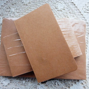 May include: Three brown notebooks of different sizes stacked on top of each other. The notebooks are wrapped in clear plastic.