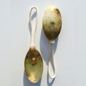 May include: Two oval-shaped bath poufs with a white string attached. The poufs are made of a light green material and have a brown, textured surface.