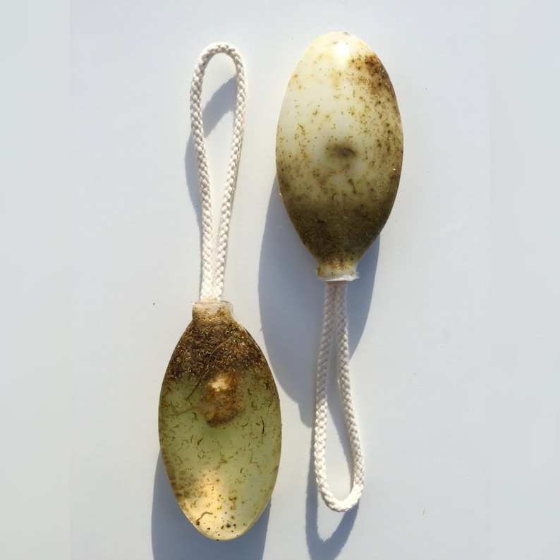 May include: Two oval-shaped bath poufs with a white string attached. The poufs are made of a light green material and have a brown, textured surface.