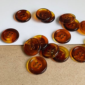 Peut inclure: Un groupe de boutons de couleur ambre avec quatre trous chacun. Les boutons sont disposés en demi-cercle sur une surface blanche et une surface brune.