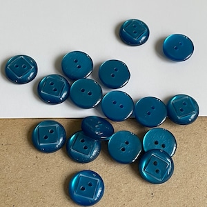 Puede incluir: Una colección de 14 botones de plástico azul turquesa con un diseño cuadrado en el centro. Algunos botones tienen dos agujeros, mientras que otros tienen cuatro.