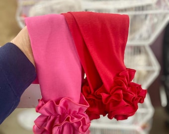 May include: Two pairs of leggings, one in bright pink and the other in red. Both leggings have ruffled trim at the ankles. The leggings are made of a soft, stretchy material.