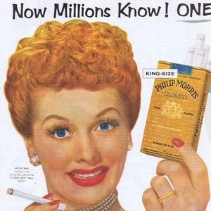 May include: A woman with red hair is smiling and holding a pack of Philip Morris King Size cigarettes. The pack is gold and blue with the text "King Size" and "Philip Morris" in white. The woman is wearing a pearl necklace and a blue dress.