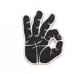 Könnte beinhalten: Schwarzer gestickter Bügelaufkleber einer Hand, die das OK-Zeichen macht.