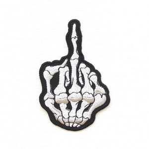 Peut inclure: Un patch brodé noir et blanc d'une main de squelette faisant un doigt d'honneur.
