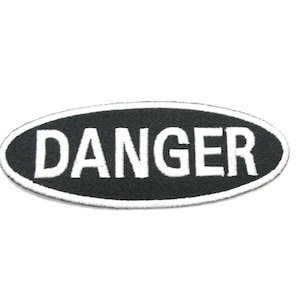 Puede incluir: Parche ovalado negro con texto bordado en blanco que dice "DANGER".