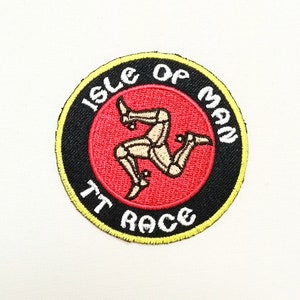 May include: A round, black and yellow embroidered patch with the text "Isle of Man TT Race" and a red background featuring the Isle of Man's three-legged symbol.