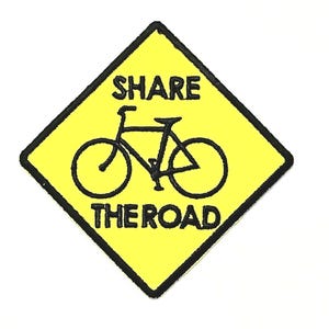 May include: A yellow diamond-shaped sign with a black border and the words "SHARE THE ROAD" in black text. A black bicycle graphic is in the center. The sign is designed to alert drivers to share the road with cyclists.