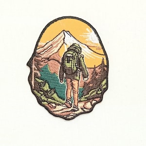 Puede incluir: Parche bordado con un excursionista con una mochila caminando por un sendero hacia la cima de una montaña. La escena se desarrolla en un cielo de puesta de sol con un degradado amarillo y naranja.