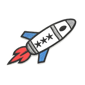 May include: A white rocket with three black stars on the side, blue wings, and a red flame. The rocket is flying to the right.