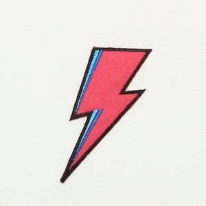 May include: A red lightning bolt patch with blue outline. The patch is iron-on and can be used to decorate clothing, bags, or other items.