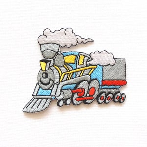 May include: Embroidered iron-on patch of a blue and grey cartoon steam train with red wheels and yellow details. The train has a smiling face and is emitting grey smoke.