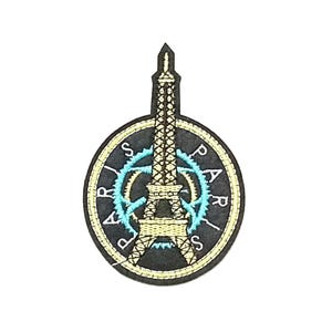Peut inclure: Patch brodé noir et or représentant la tour Eiffel avec un motif circulaire bleu et blanc autour. Le texte "PARIS" est brodé autour du motif circulaire.