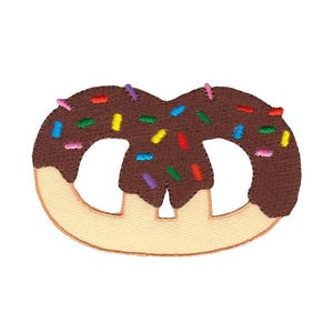 May include: Embroidered patch of a pretzel with chocolate frosting and colorful sprinkles. The pretzel is light tan with a dark brown chocolate coating and various colored sprinkles.