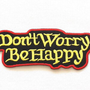 May include: Yellow embroidered text on a black patch with a red border that reads "Don't Worry Be Happy".