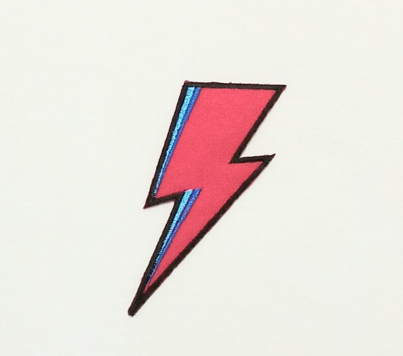 May include: A red lightning bolt patch with a blue outline. The patch is iron-on and can be used to decorate clothing, bags, or other items.