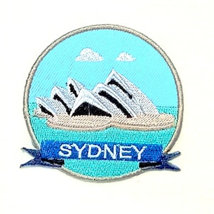 Op de afbeelding: Een ronde, blauwe en witte geborduurde patch met een afbeelding van het Sydney Opera House en het woord "SYDNEY" op een blauwe banner.