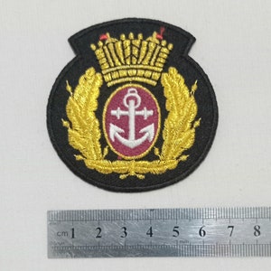 May include: Black embroidered patch featuring a gold crown, laurel leaves, and a central emblem with a white anchor on a burgundy background. The patch is approximately 3 inches in diameter.