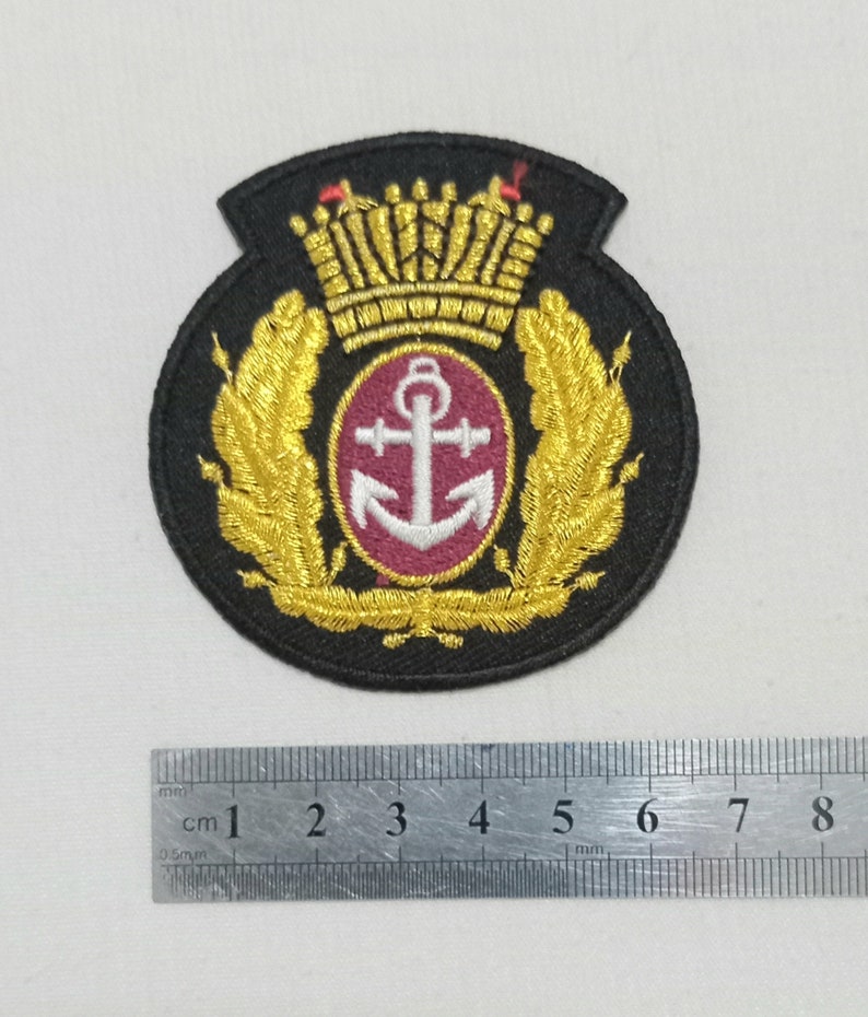 May include: Black embroidered patch featuring a gold crown, laurel leaves, and a central emblem with a white anchor on a burgundy background. The patch is approximately 3 inches in diameter.