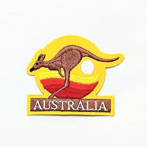 Può includere: Toppa ricamata gialla con un canguro che salta davanti a un sole rosso, giallo e bianco. Il testo "AUSTRALIA" è sotto il canguro.