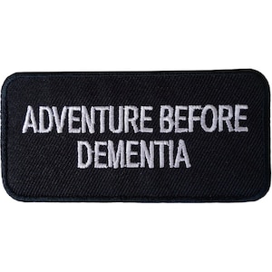 May include: Black rectangular patch with white embroidered text that reads "Adventure Before Dementia".