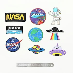 Peut inclure: Un ensemble de dix patchs thermocollants sur le thème de l'espace. Les patchs sont colorés et comprennent des images de planètes, d'astronautes, de vaisseaux spatiaux et du logo de la NASA.
