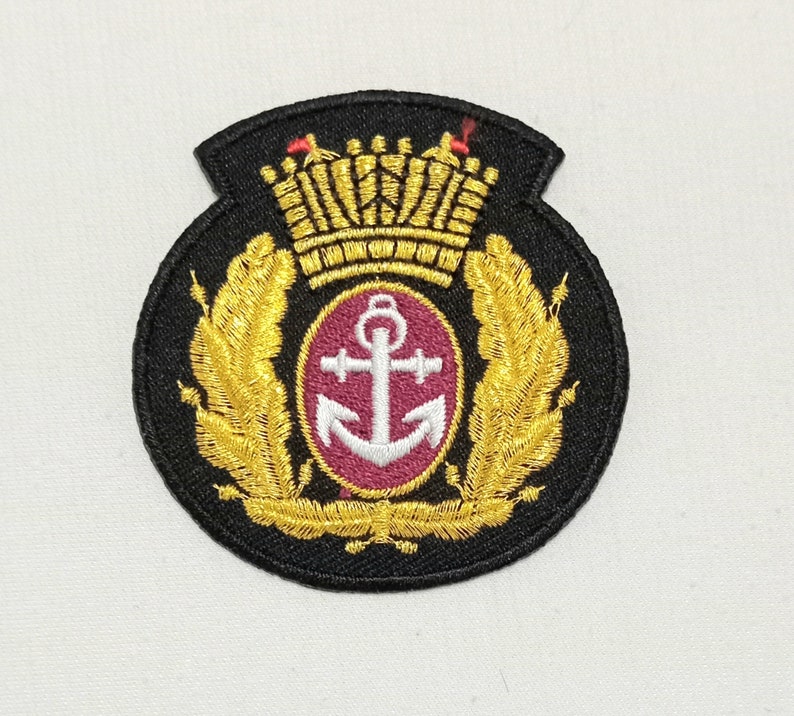 May include: Embroidered patch featuring a gold crown, laurel leaves, and an anchor emblem on a black background. The anchor is white, set within a burgundy circle. The patch has a shield-like shape.