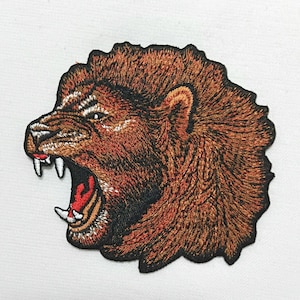 May include: Embroidered patch of a roaring lion's head with a brown and orange mane. The lion's mouth is open, showing sharp teeth and a red tongue.