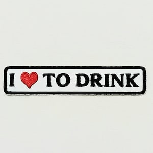 May include: A rectangular patch with the phrase "I ❤️ TO DRINK" in black capital letters. A red heart replaces the word "love". The patch has a black border and is set against a white background.