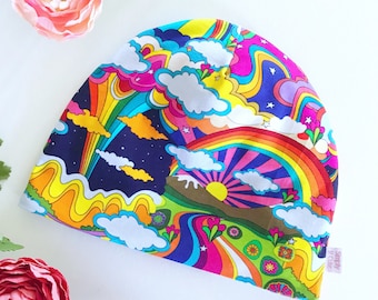 May include: A colorful beanie hat with a psychedelic rainbow, cloud, and star pattern. The hat has a white background with bright pink, yellow, blue, green, and orange accents. The text "Simply Cute" is printed on the side of the hat.