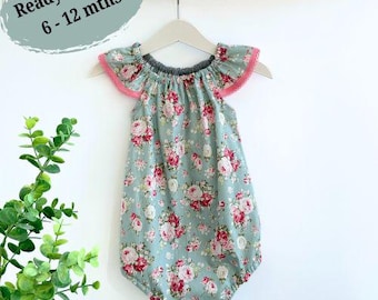 Puede incluir: Un body de bebé azul claro con estampado floral y ribete rosa en las mangas. El body tiene un escote con volantes y está listo para enviar para bebés de 6 a 12 meses.