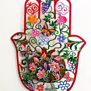 Könnte beinhalten: Eine rote Hamsa-Hand aus Metall mit filigranen Ausschnitten von Blumen, Schmetterlingen, Granatäpfeln und Trauben. Das Design ist in leuchtenden Farben bemalt, darunter Pink, Blau, Grün, Gelb und Orange.
