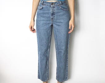 May include: A woman is wearing a light blue cropped t-shirt and blue denim jeans. She is standing on a white background.