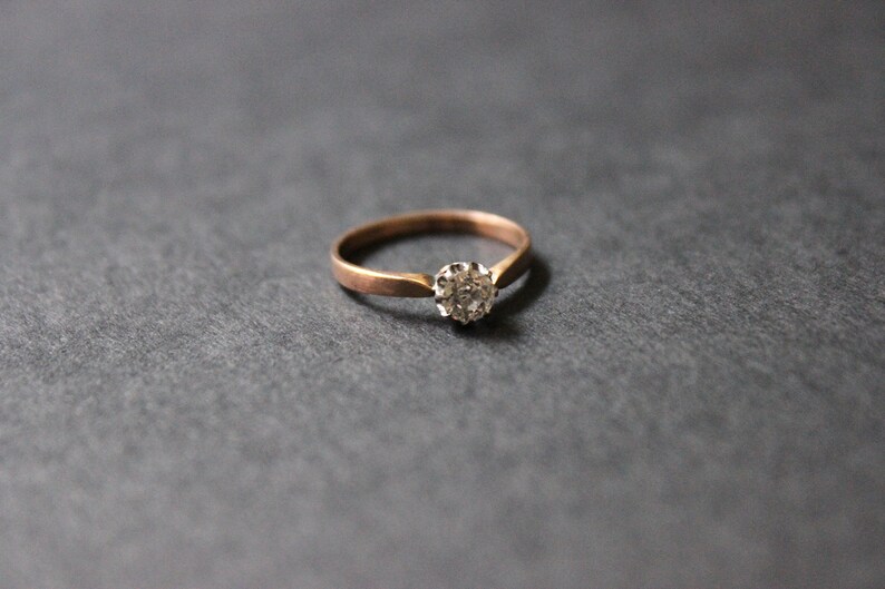 May include: A simple gold band ring with a single round diamond set in a small cluster.