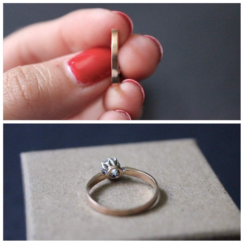 May include: A gold engagement ring with a single round diamond set in a prong setting. The ring is on a brown surface.