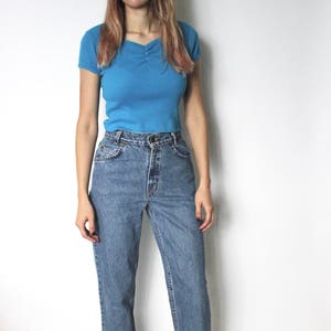 May include: A woman wearing a light blue short-sleeved shirt and blue denim jeans. She is wearing brown sandals.