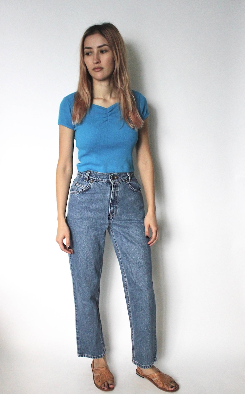 May include: A woman wearing a light blue short-sleeved shirt and blue denim jeans. She is wearing brown sandals.