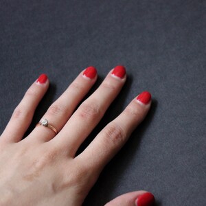 May include: A hand with red nail polish and a gold ring with a single diamond on the ring finger.