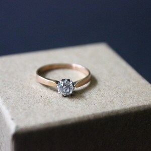 May include: A gold ring with a single round diamond set in the center.