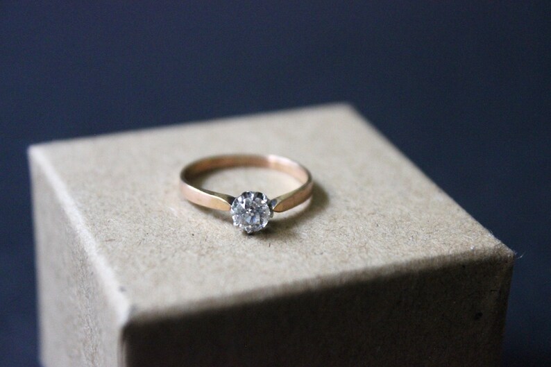 May include: A gold ring with a single round diamond set in the center.